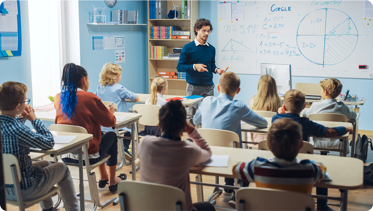 A photo of a teacher at the front of a class room full of students giving a lesson.