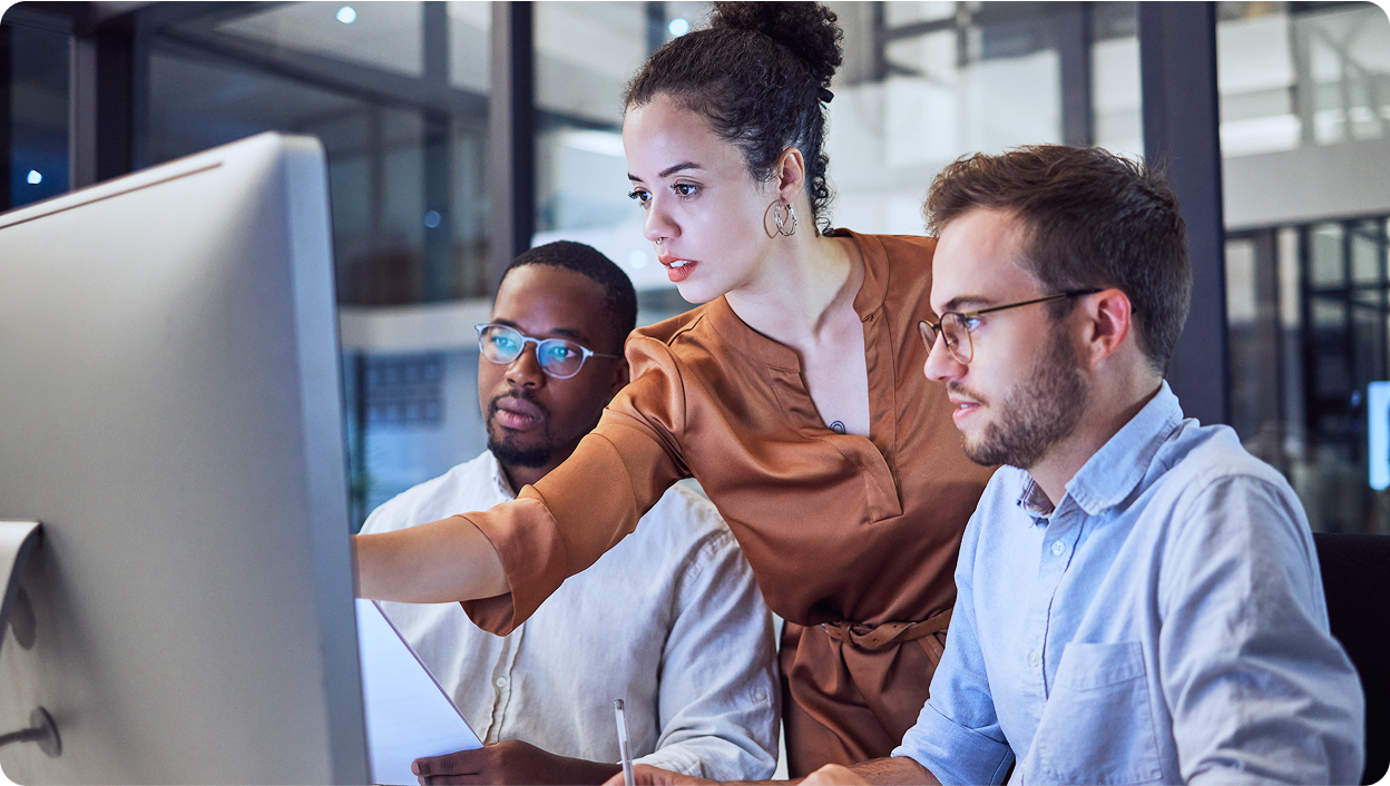 Three office workers looking at information on a desktop computer.