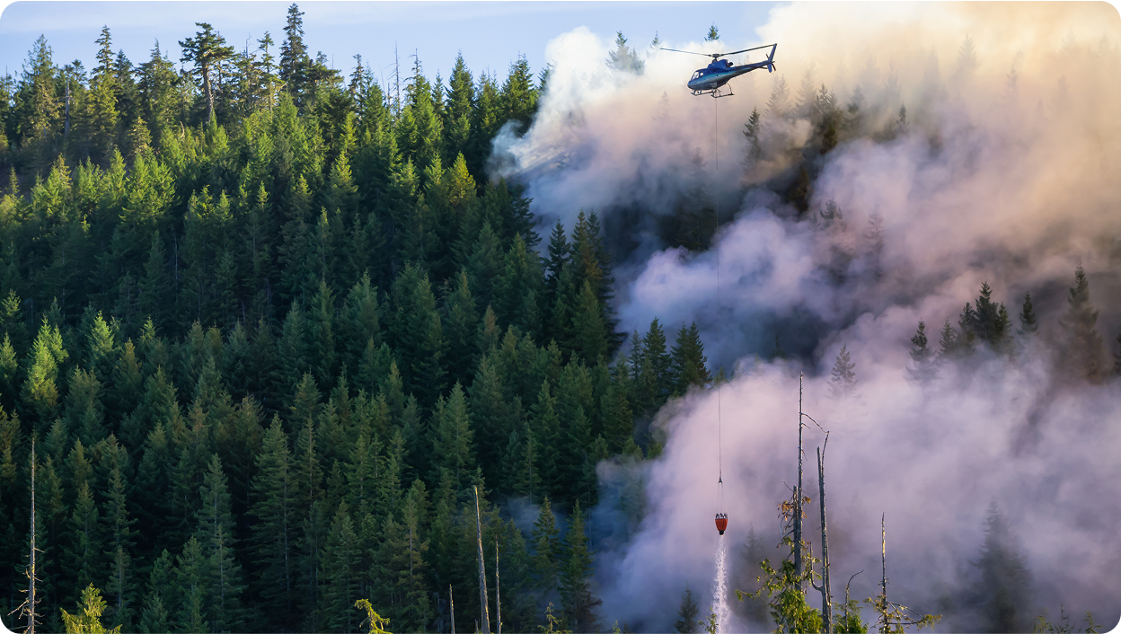 A photo of a helicopter dropping water on a wildfire burning in Alberta.